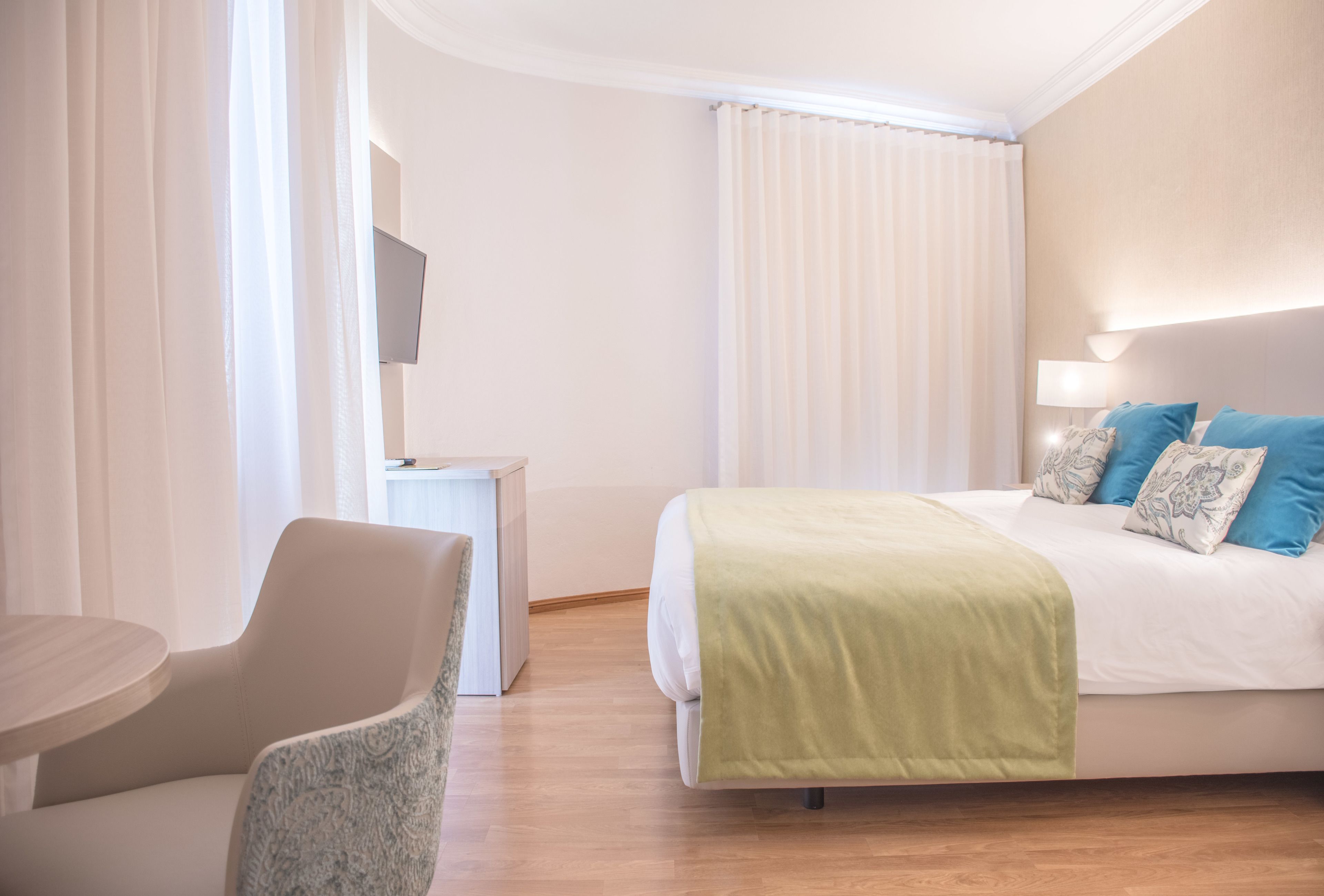Una habitación de hotel con una cama, una silla, una mesita pequeña y un televisor en la pared.