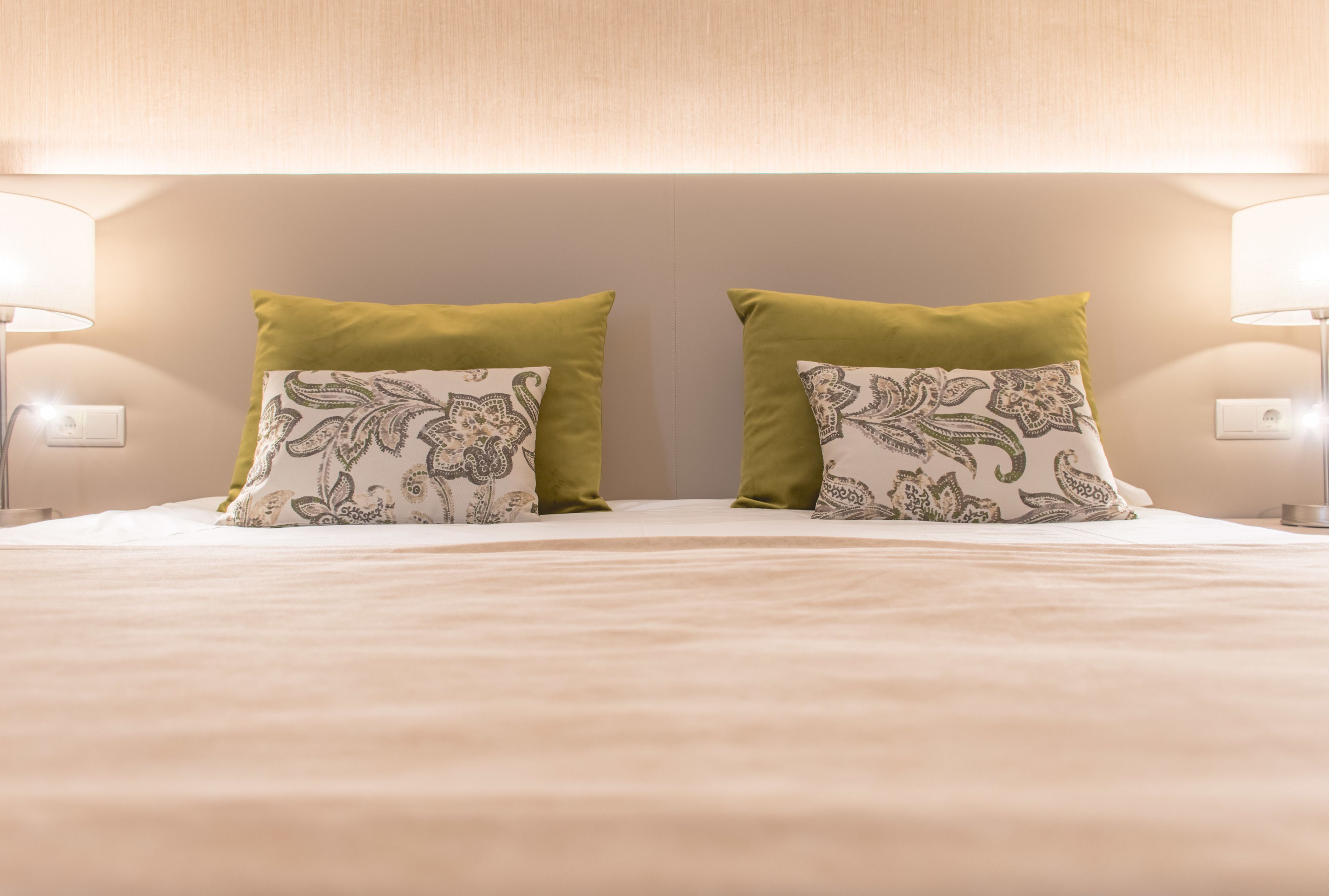 Una cama bien tendida con dos almohadas decorativas, una lámpara de noche y un interruptor de pared.