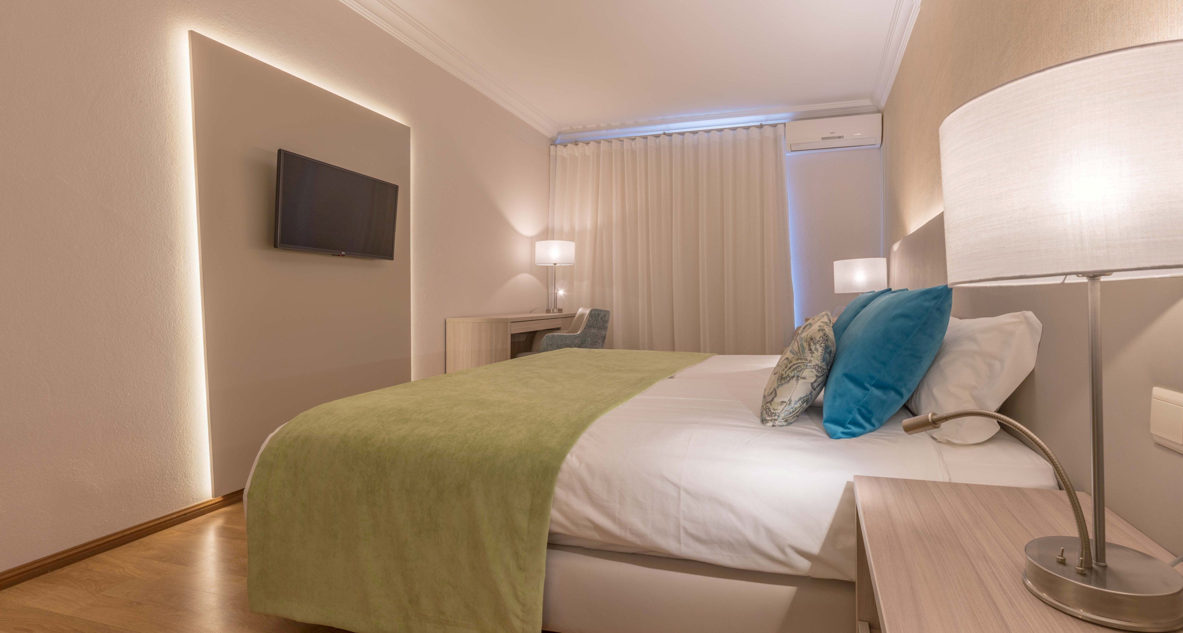 A hotel room with a bed, bedside lamps, a flat-screen TV, and a window with curtains.