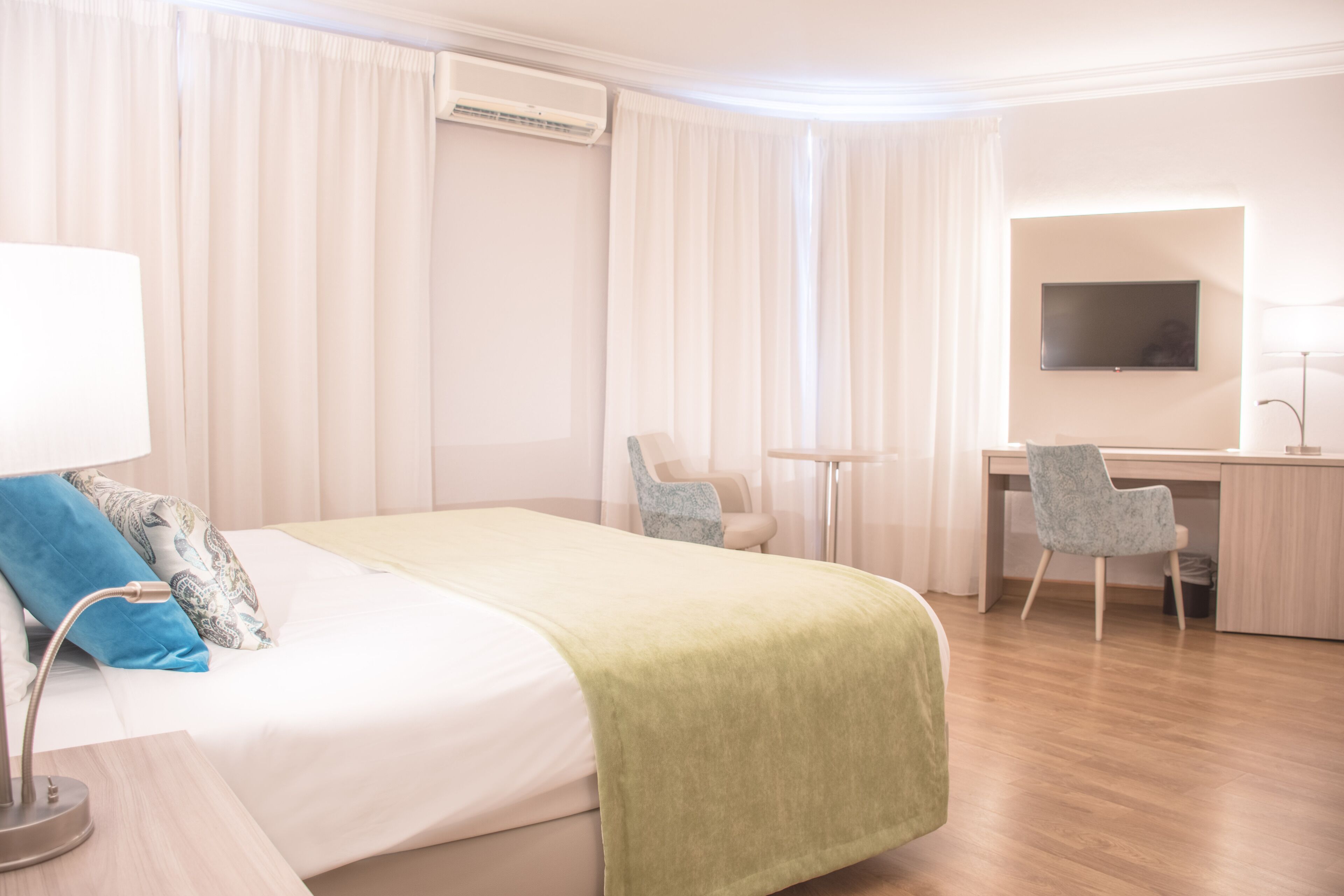 Hotellihuone, jossa on sänky, työpöytä, tuoli, televisio ja ilmastointilaite.