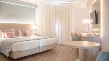 A hotel room with a double bed, a round table, a chair, a desk, a TV, and a window with curtains.