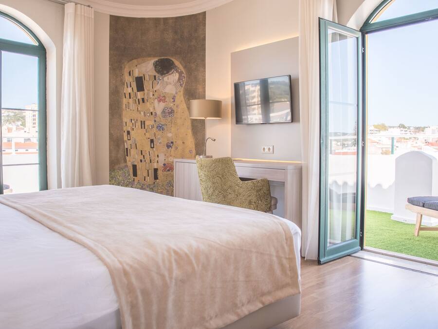 Ein Hotelzimmer mit einem großen Bett, einem an der Wand montierten Fernseher und Blick auf die Stadt durch die offene Tür.
