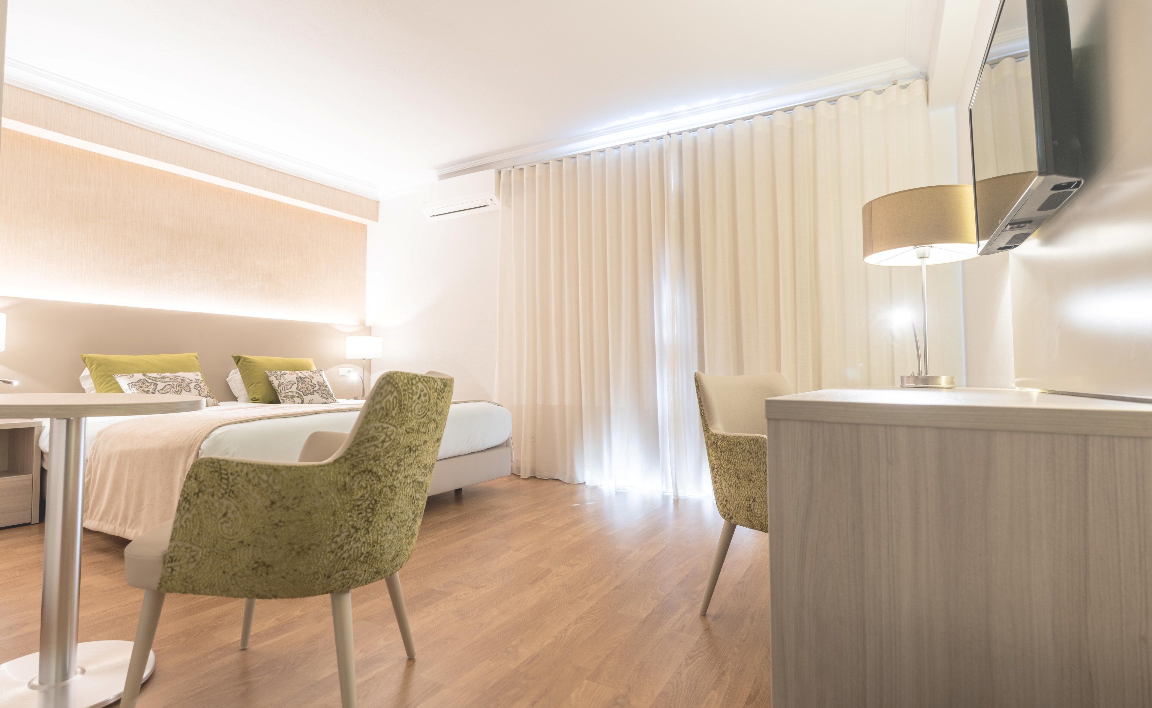 Una camera d'albergo con un letto, due sedie, una scrivania, una televisione e una finestra con tende.
