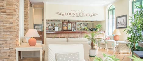 Eine Lounge-Bar mit Steinwand, weißen Möbeln und einer Bar, die mit verschiedenen Flaschen bestückt ist.