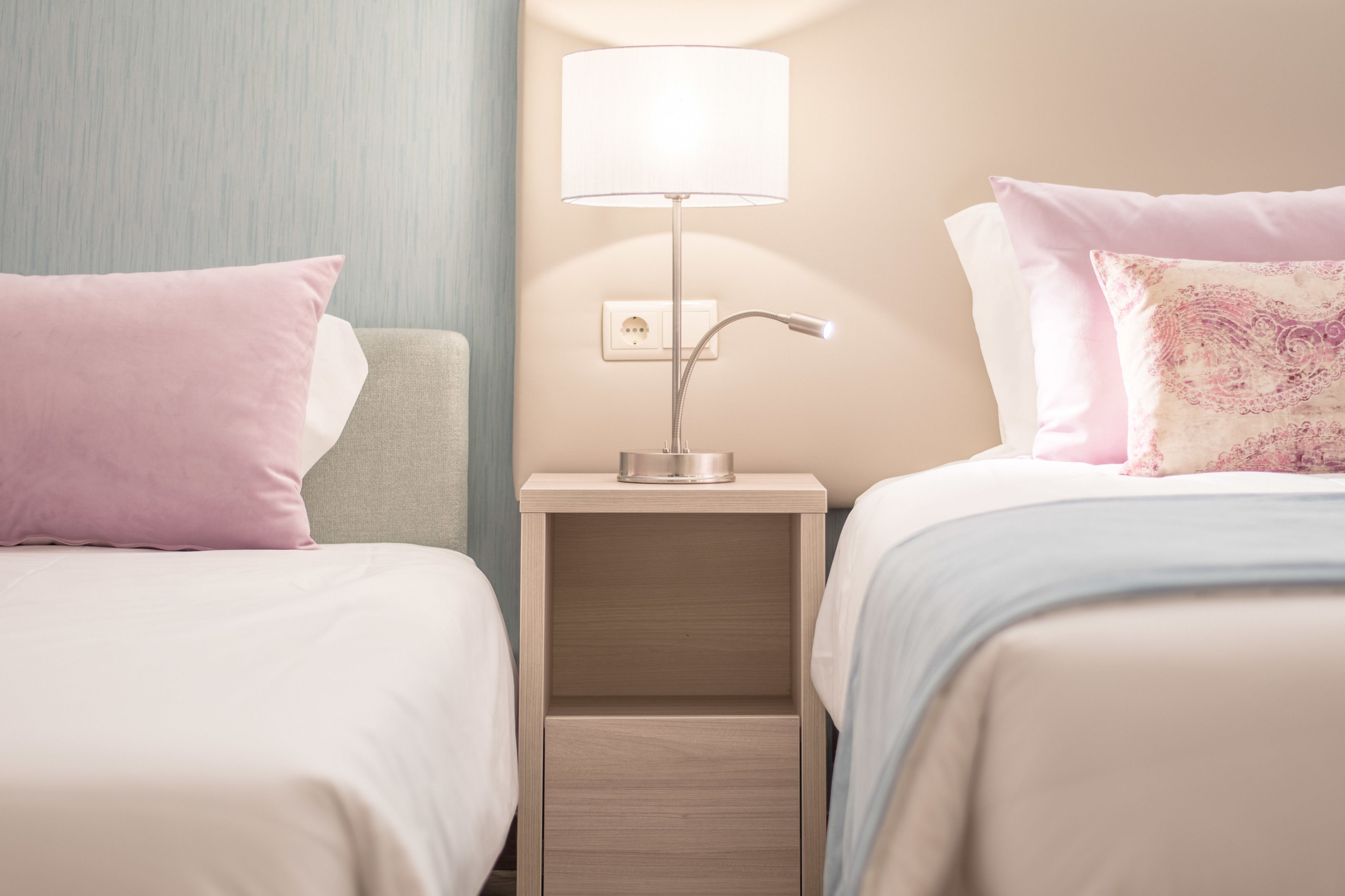 A hotel room with two beds, a nightstand with a lamp, and a wall socket.