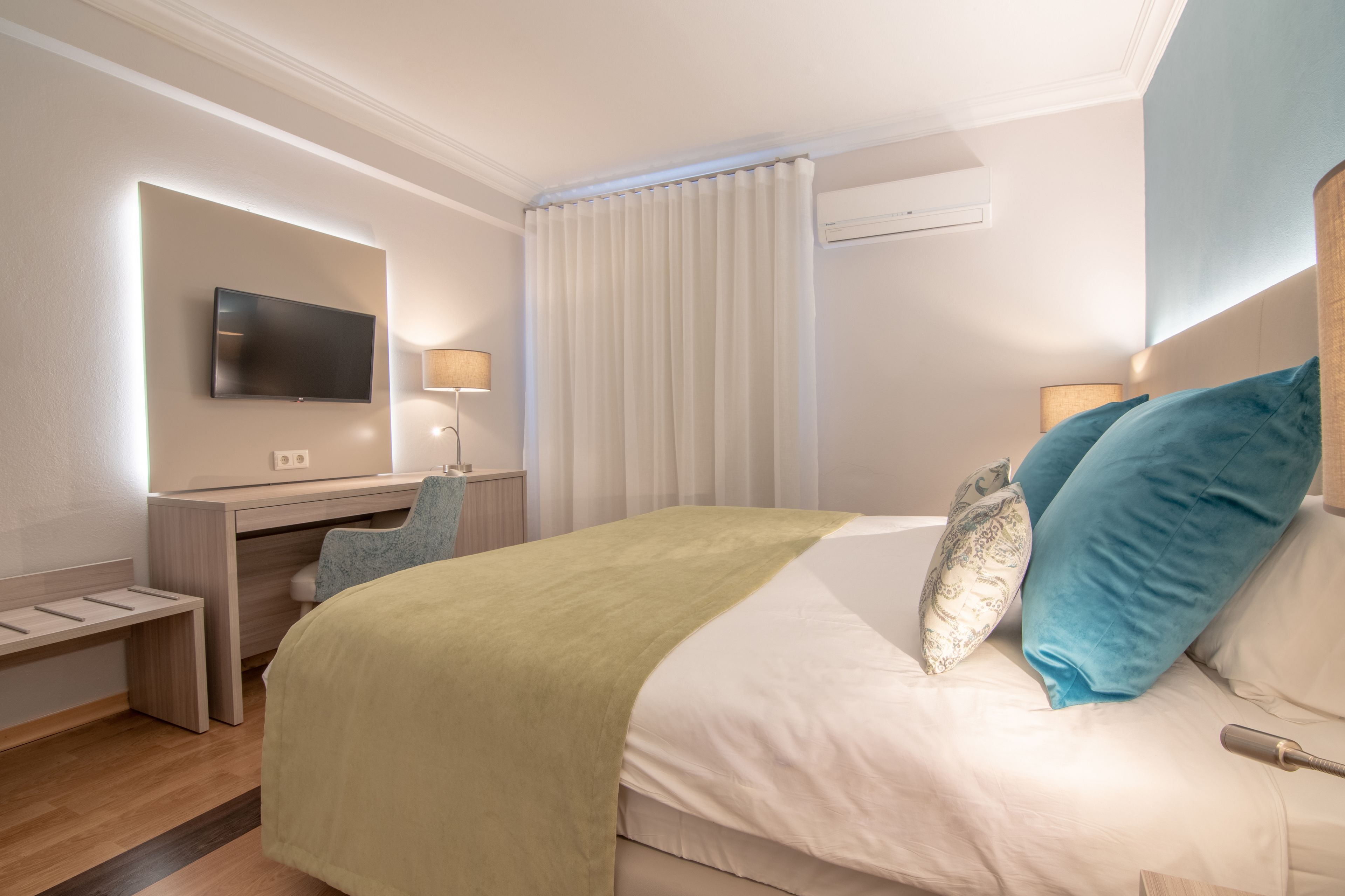 A hotel room with a bed, a desk, a TV, and a window with curtains.