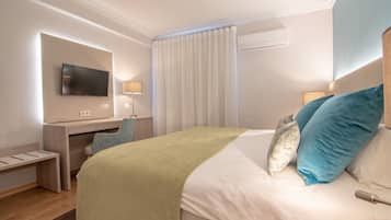 Una habitación de hotel con cama, escritorio, televisor y ventana con cortinas.