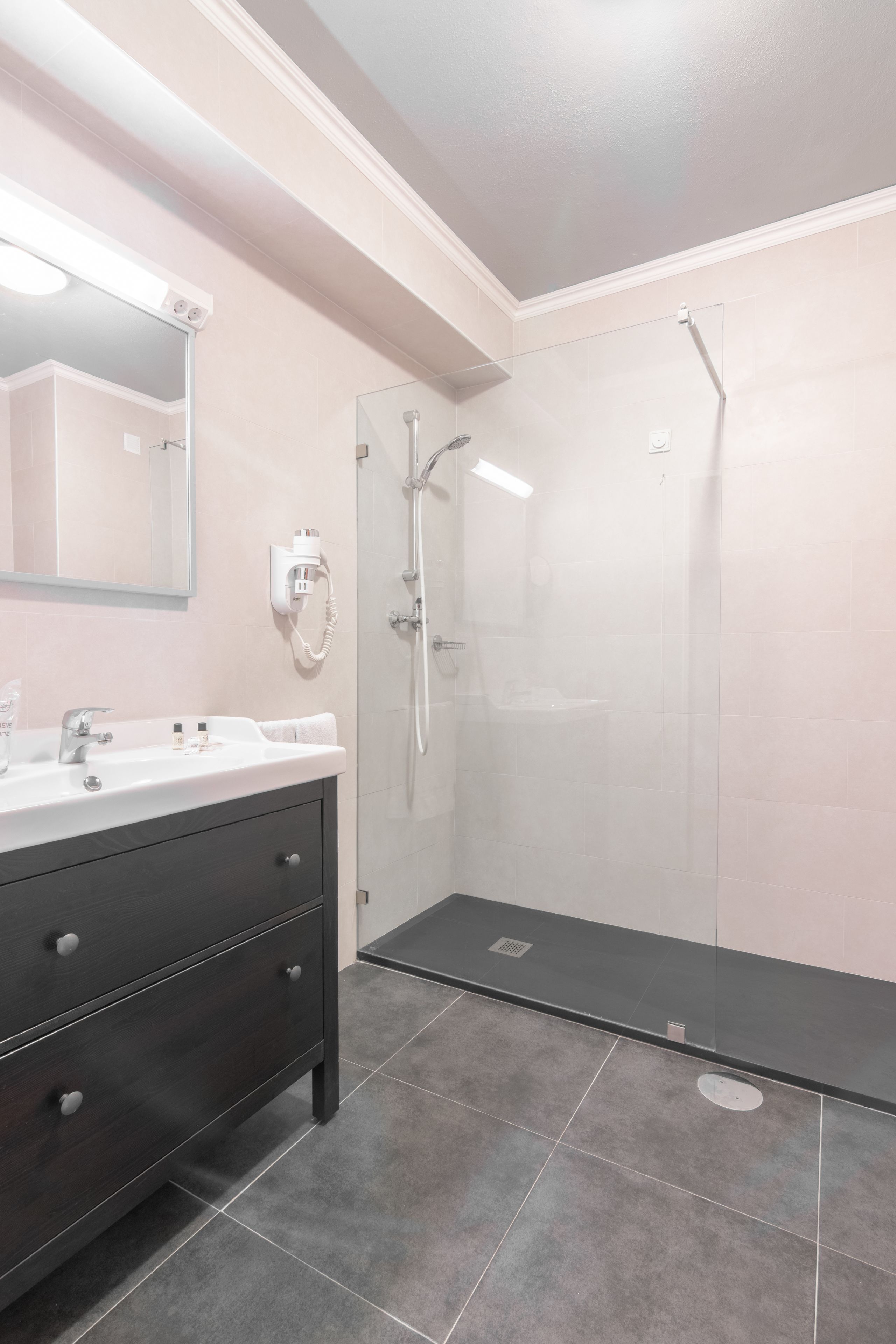 Een moderne badkamer met een donker houten wastafelmeubel, een witte wasbak en een douche met glazen wanden.