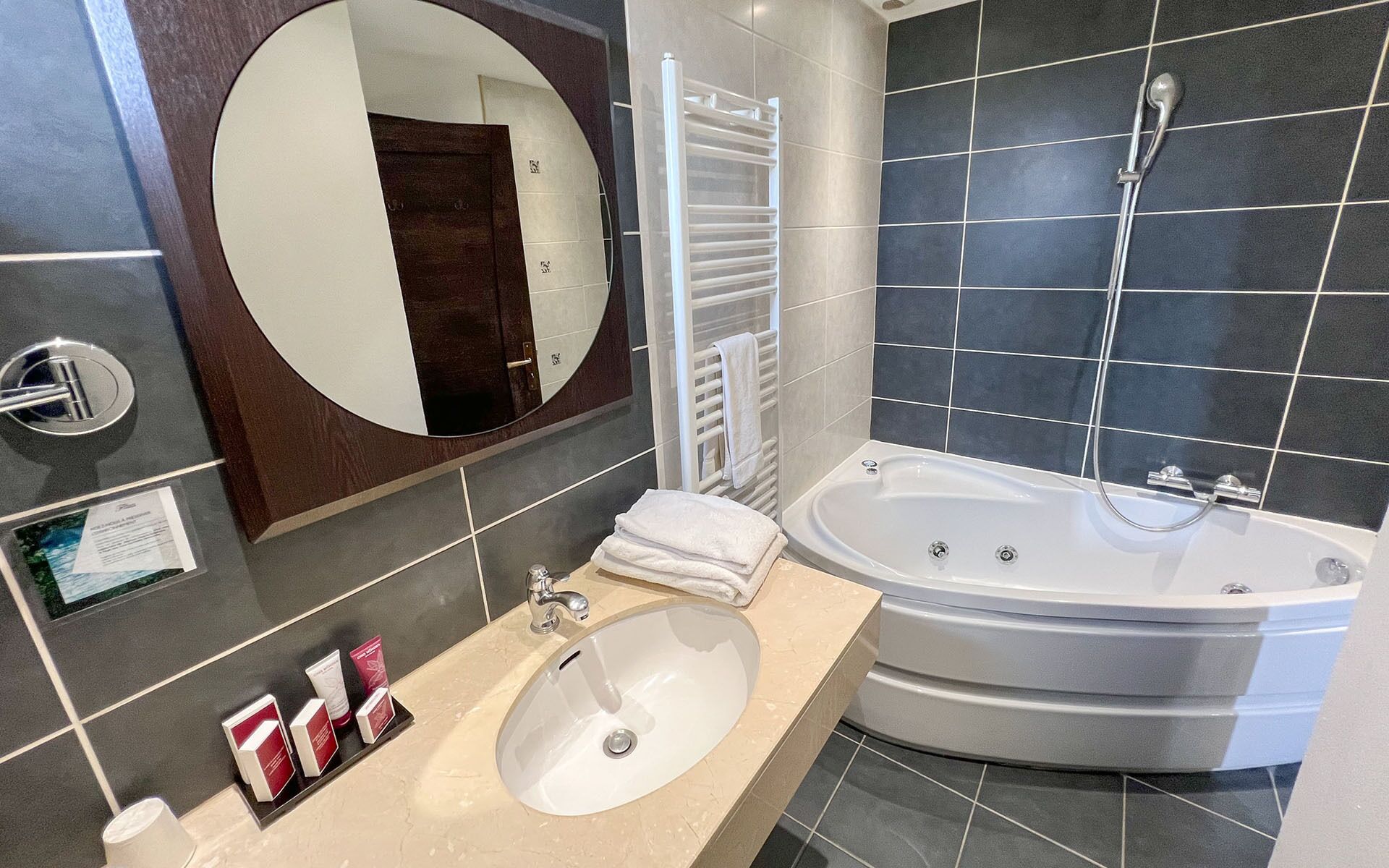 A modern bathroom with a large bathtub, a round mirror, and a sink with toiletries.