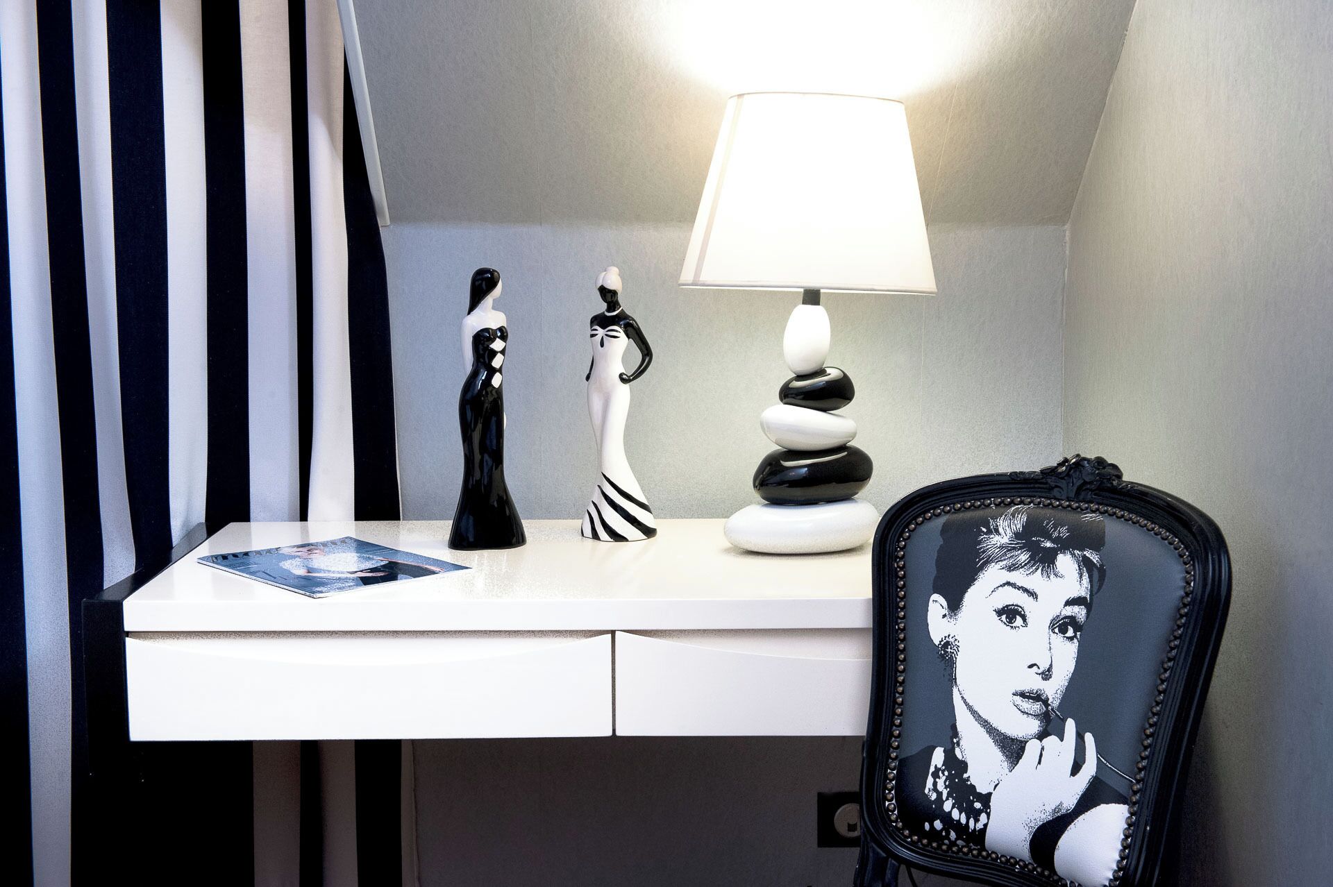 Een bureau met een lamp, twee beeldjes, een stapel stenen en een stoel met een grafisch ontwerp.