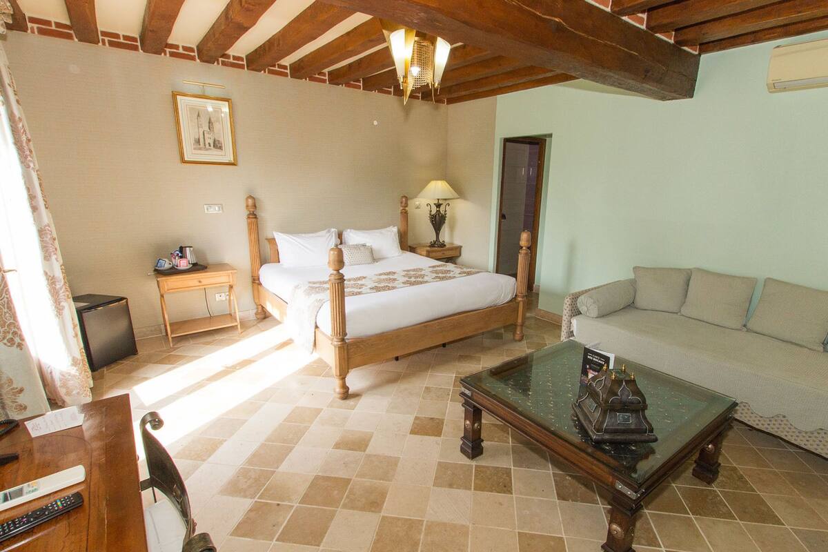 Un dormitorio con cama, mesitas de noche, un sofá, una mesa de centro de vidrio y un cuadro en la pared.
