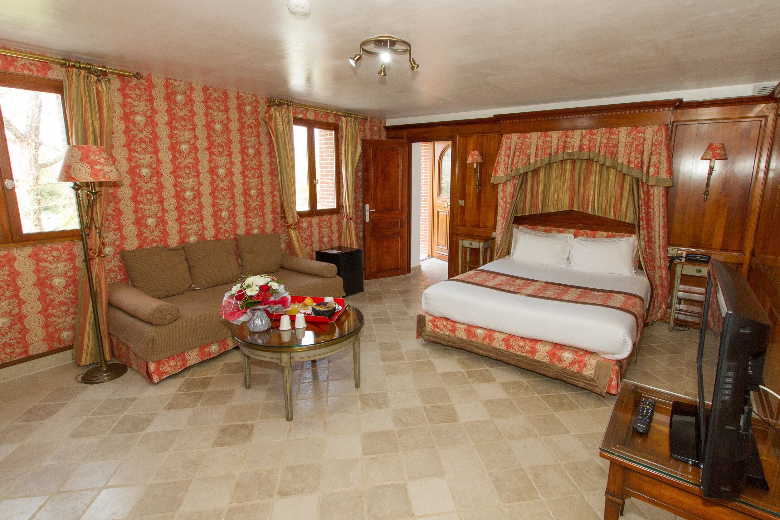 A hotel room with a sofa, a bed, a coffee table with flowers, and a TV.