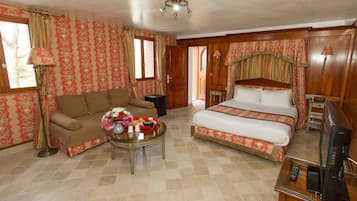 A hotel room with a sofa, a bed, a coffee table with flowers, and a TV.