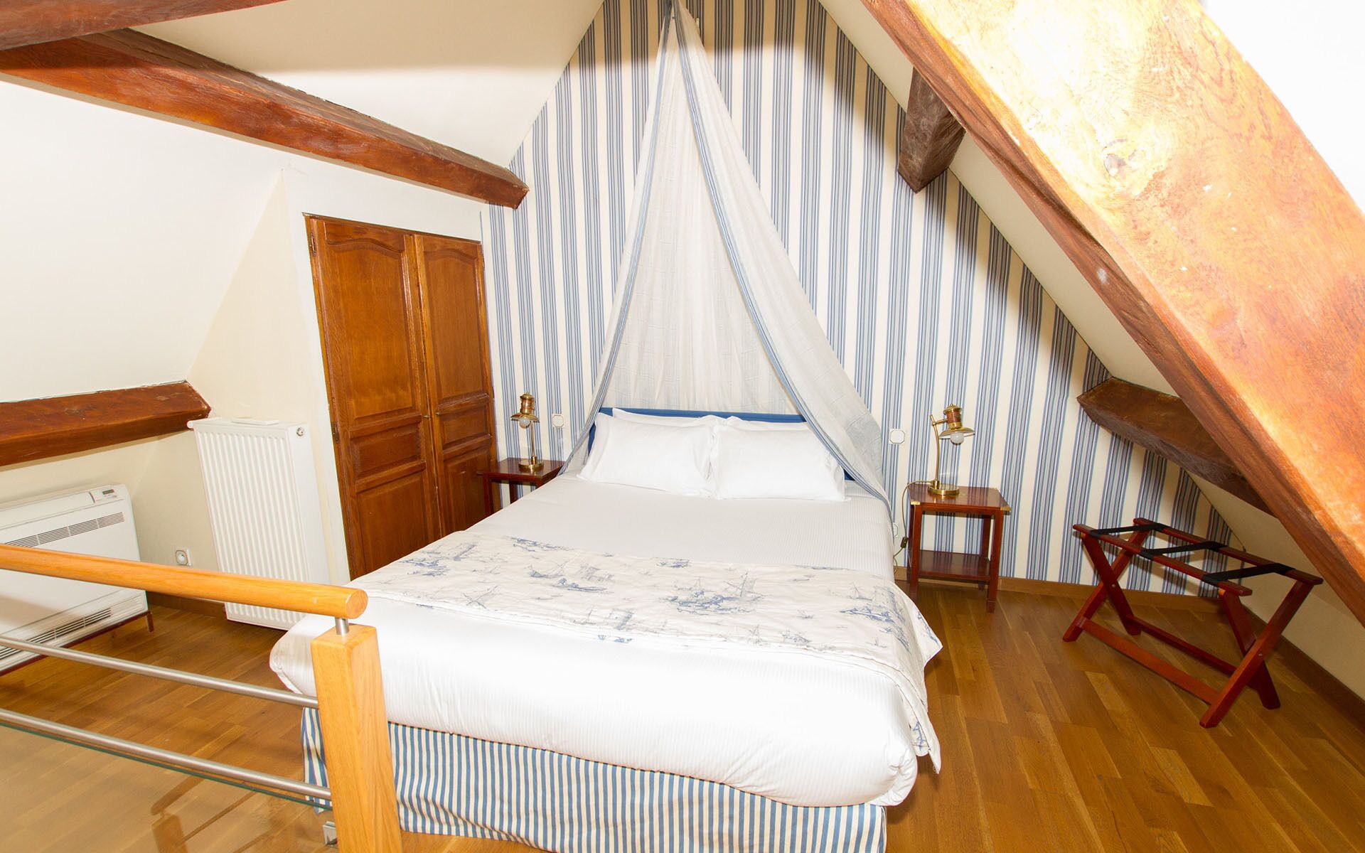 A bedroom with a bed, wooden headboard, striped wallpaper, a window with a curtain, a radiator, and a wooden ladder.