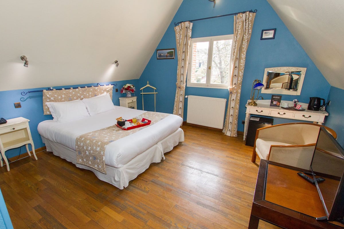 Un dormitorio con cama, mesitas de noche, cómoda, silla, ventana con cortinas y radiador.