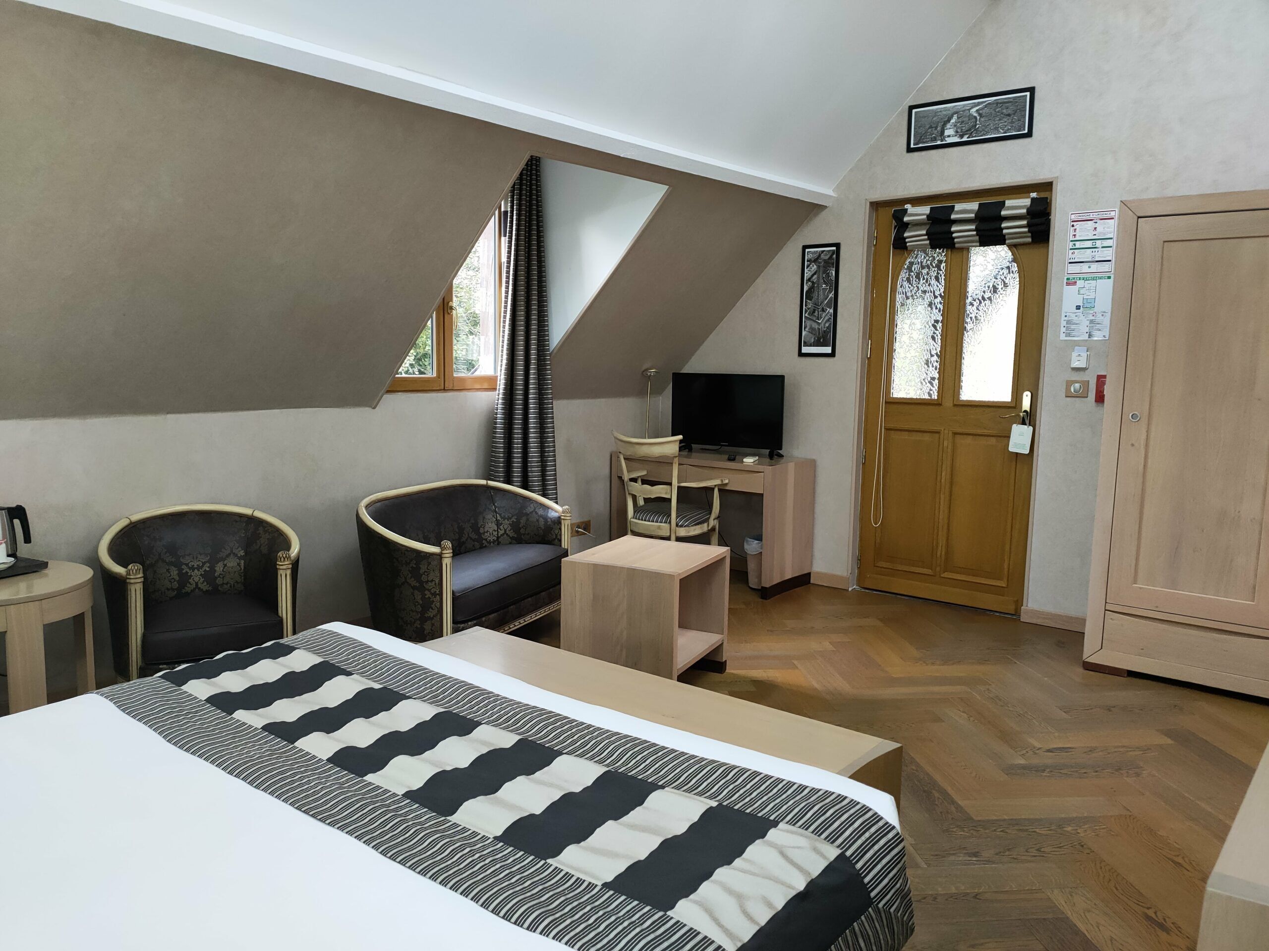 A bedroom with a bed, two chairs, a desk with a computer, a television, and a door with a window.