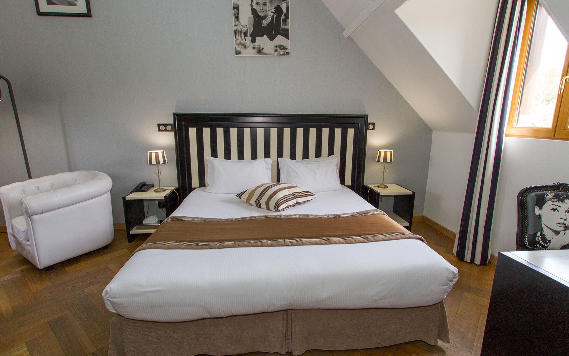 A neatly arranged bedroom with a large bed, a bedside table with a lamp, a chair, and a framed picture on the wall.