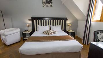 A neatly arranged bedroom with a large bed, a bedside table with a lamp, a chair, and a framed picture on the wall.