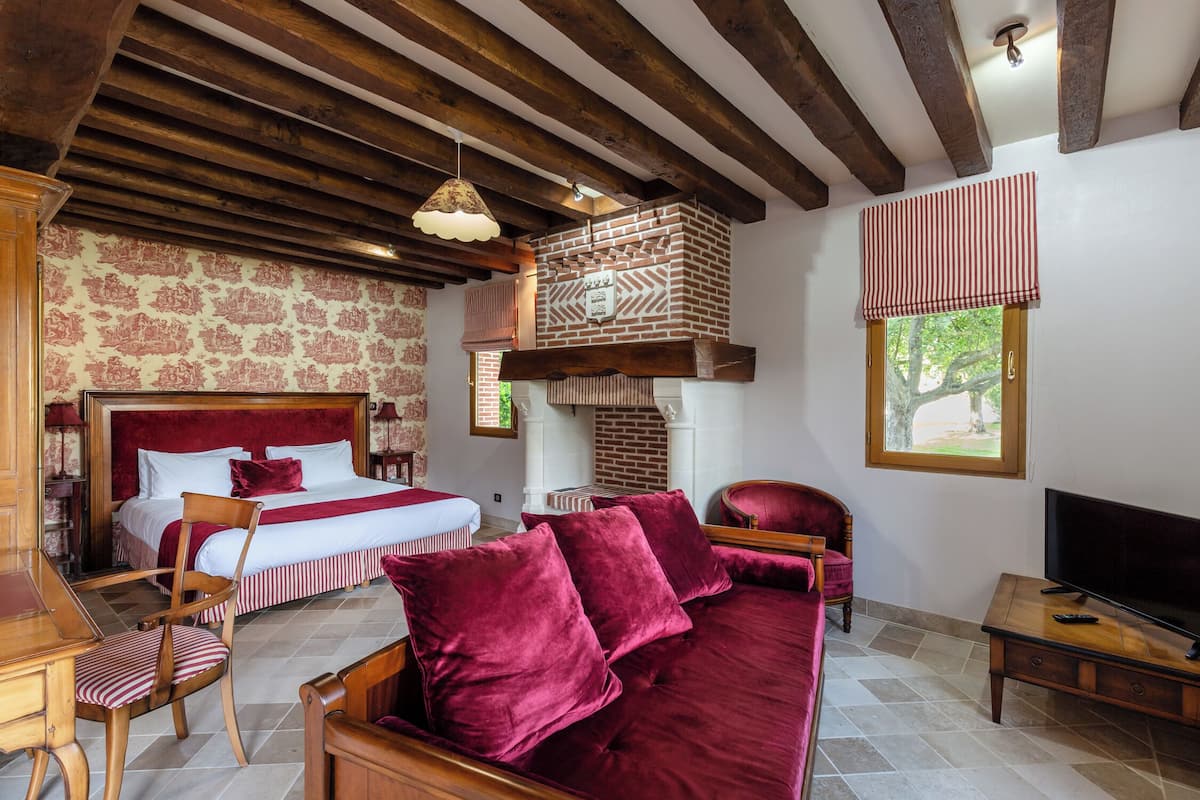 Un dormitorio con una cama grande, una silla de madera, un sofá rojo, un televisor y una chimenea.