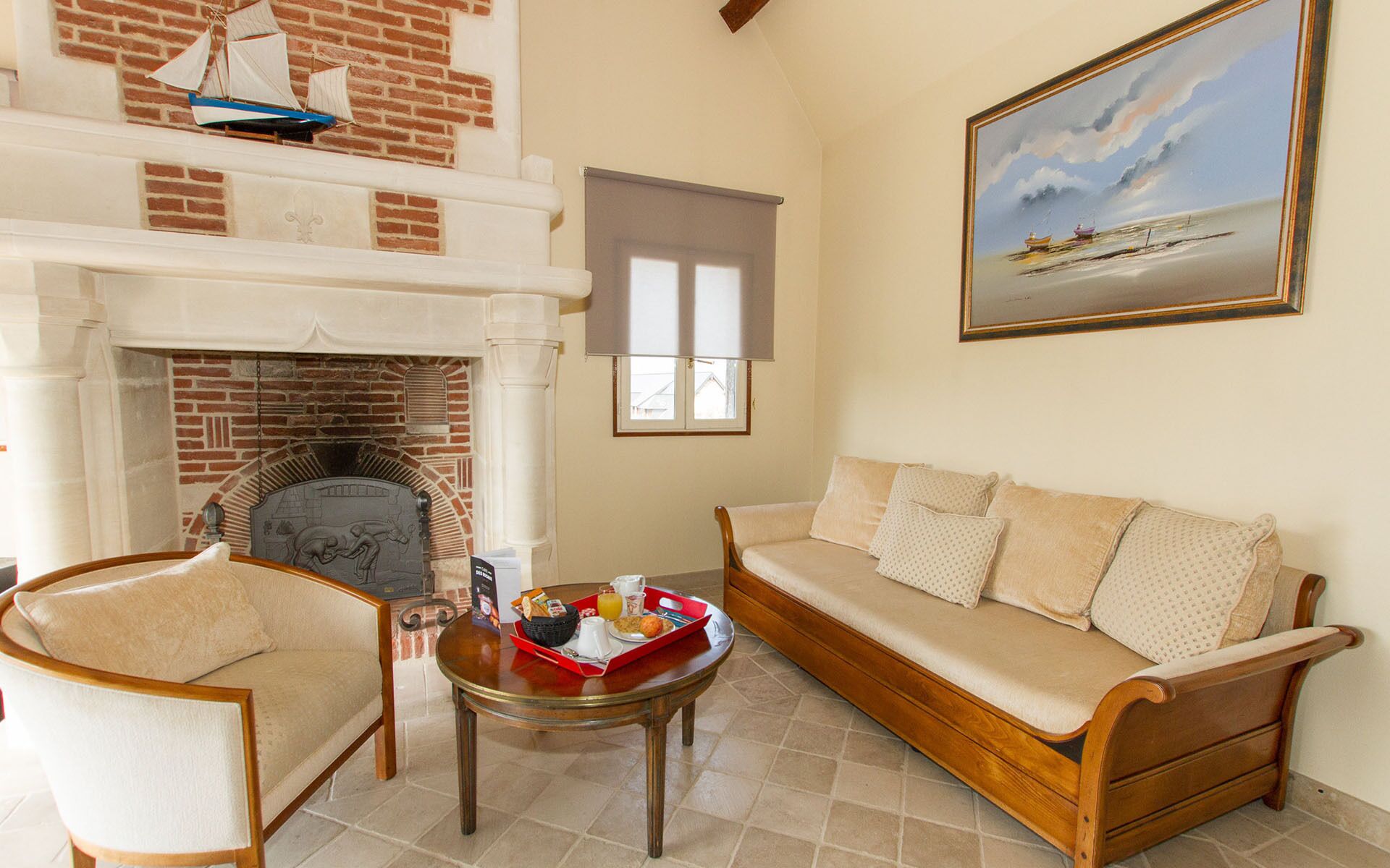 A living room with a fireplace, a sofa, a coffee table with breakfast items, and a painting of a beach scene.