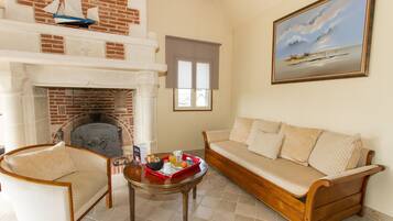 A living room with a fireplace, a sofa, a coffee table with breakfast items, and a painting of a beach scene.