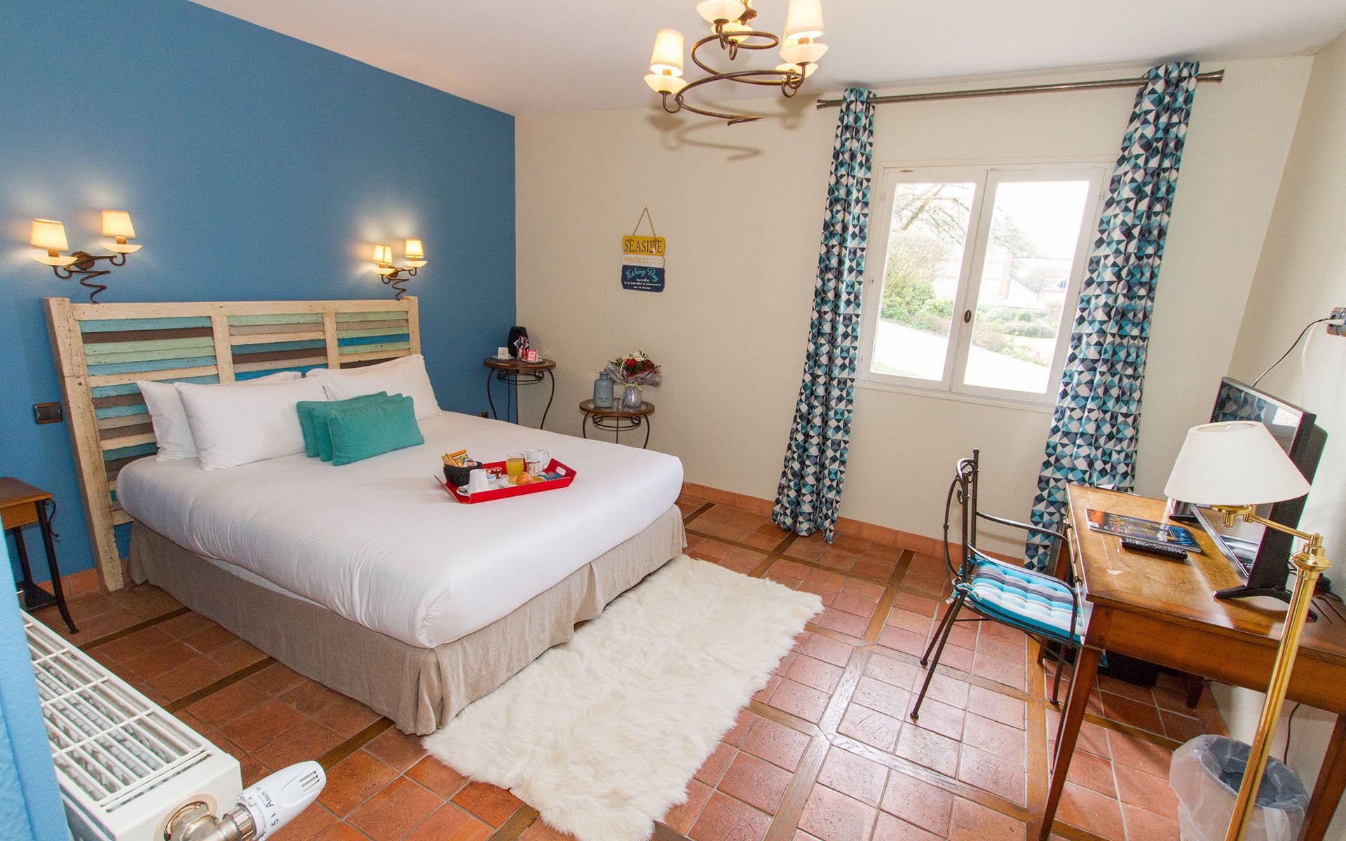 Un dormitorio con cama, mesita de noche, silla, escritorio, radiador, cortinas y ventana.