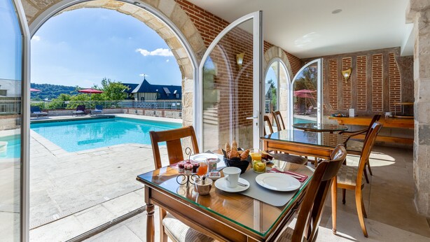 Un coin repas avec une table en verre, des chaises et des aliments pour le petit-déjeuner. On peut apercevoir une piscine à travers les portes vitrées.