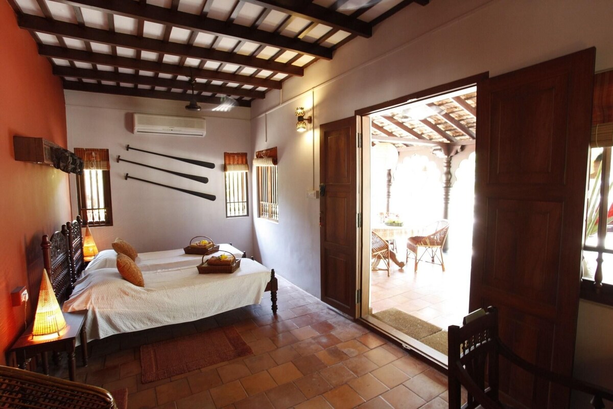 A room with a bed, a chair, a table, and a sliding door leading to an outdoor area with chairs.