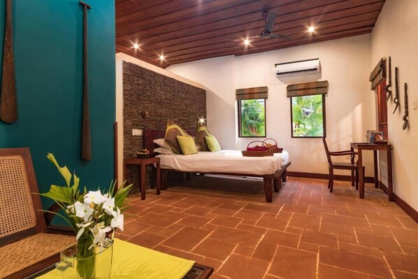 A room with a bed, a chair, a small table, and a window with a view of greenery.