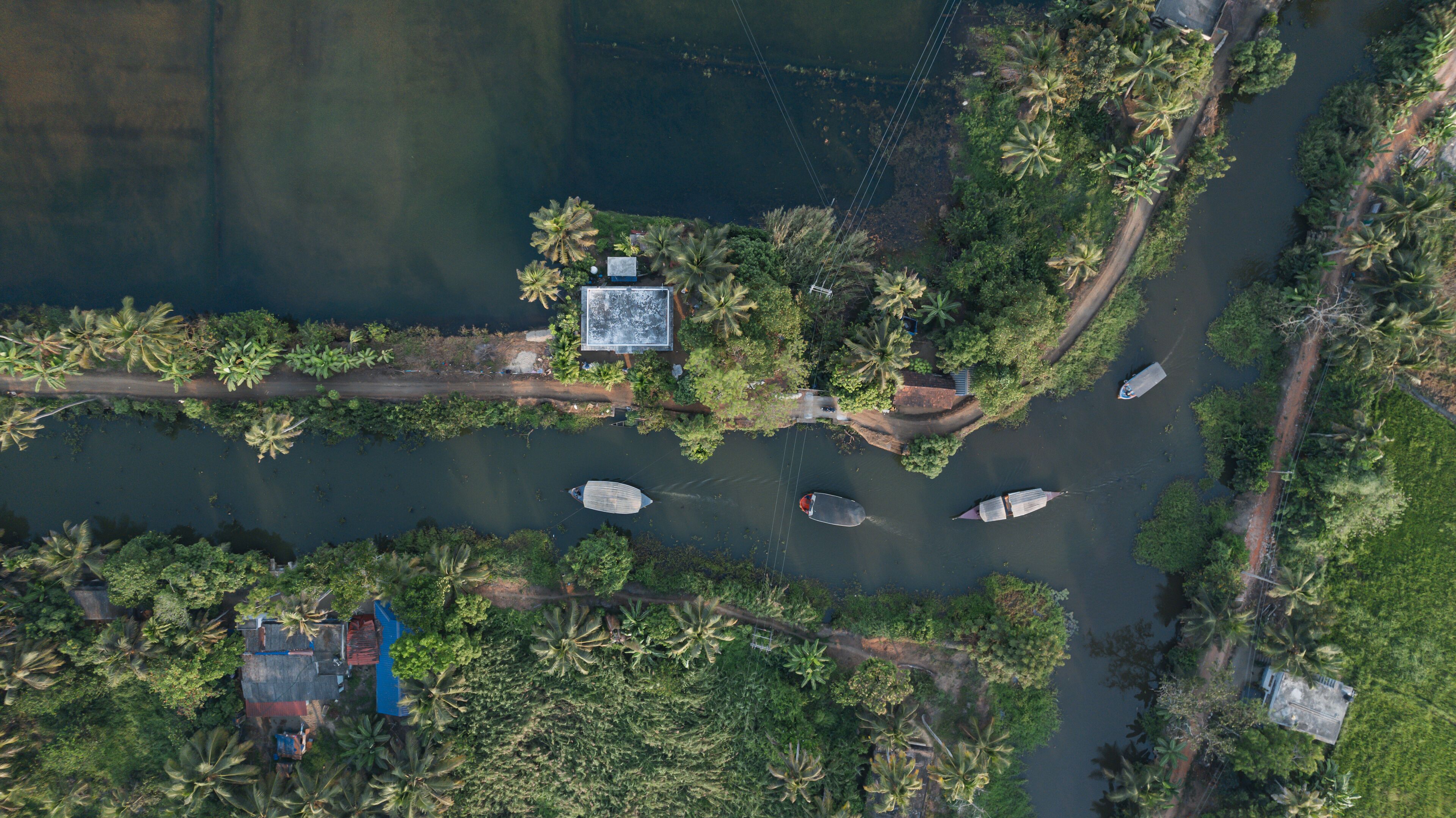 An aerial view of a riverside area with boats, a dock, and dense greenery.