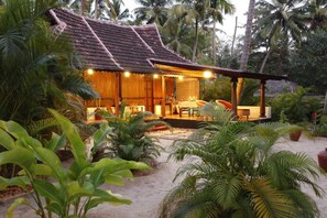 A wooden house with a tiled roof, surrounded by lush greenery and palm trees. - Amritara A Beach Symphony (Cherthala)
