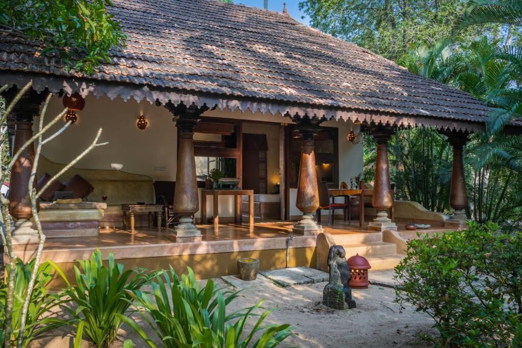 A traditional house with a tiled roof, wooden pillars, and a stone statue in the foreground.