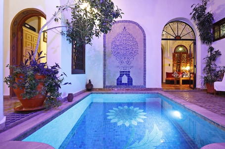 A pool with a blue mosaic floor, surrounded by a tiled patio and potted plants.