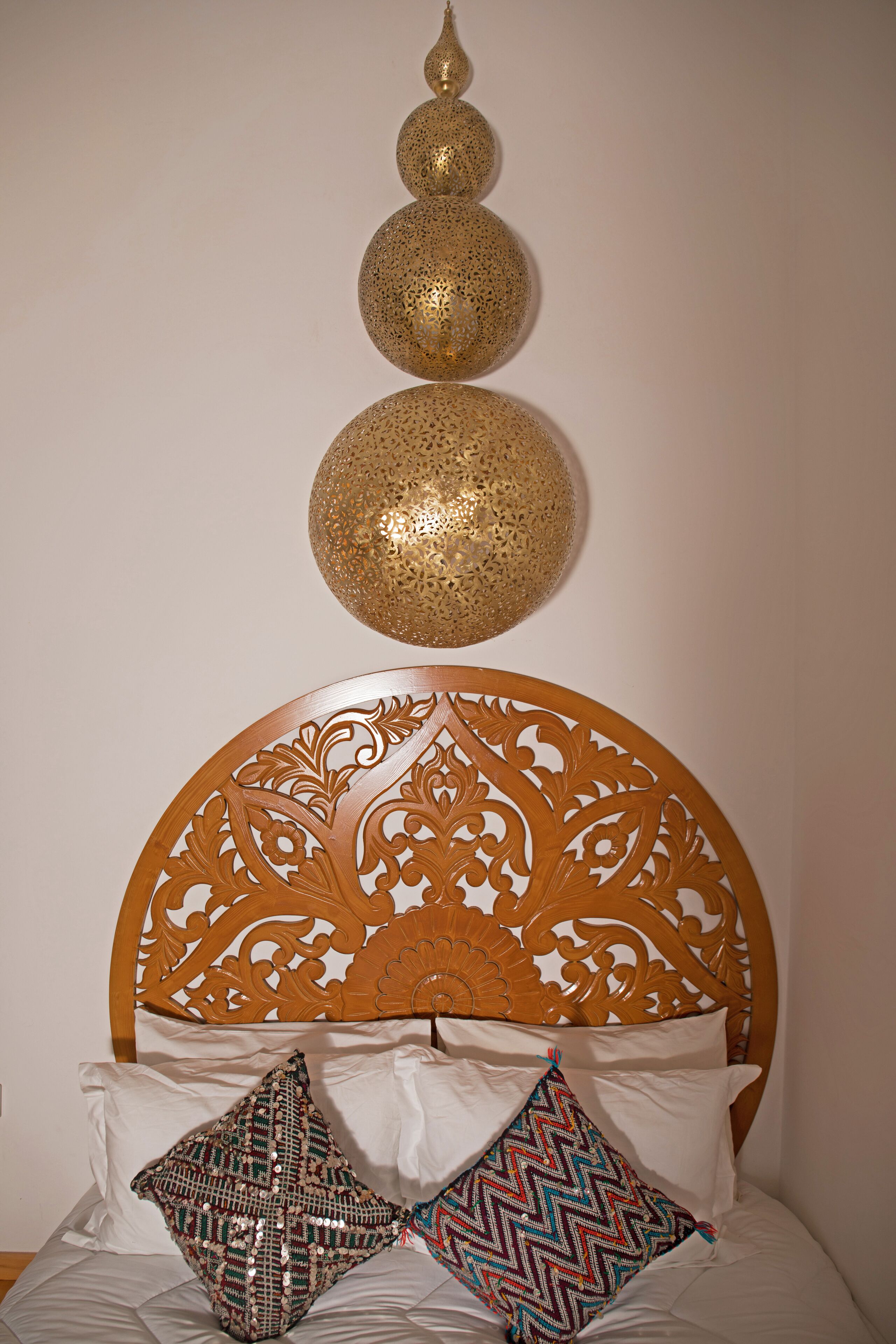 Una cama con cabecera de madera, dos esferas decorativas en la pared y almohadones estampados.
