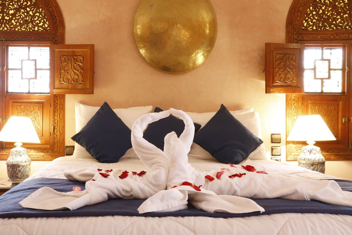 A hotel room with a bed, pillows, a decorative wall piece, and two lamps.