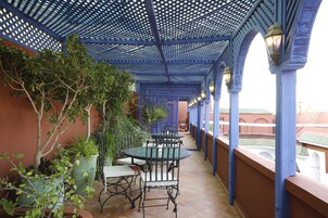Un'area esterna coperta con soffitto blu, piante in vaso, un tavolo rotondo e sedie.