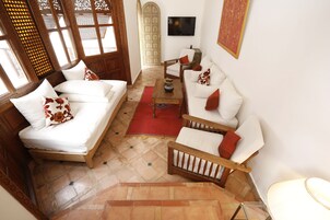 Amplia sala de estar con sofá, sillón y mesa de centro. Hay un televisor montado en la pared y una escalera que conduce a otro nivel.