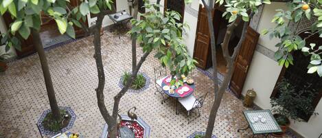 An outdoor courtyard with tiled flooring, potted plants, and tables set up for dining.