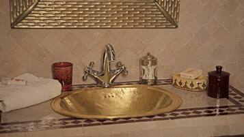 Un baño con un lavamanos dorado, un espejo y un perchero para toallas.