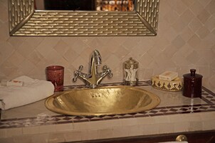 Un baño con un lavamanos dorado, un espejo y un perchero para toallas.
