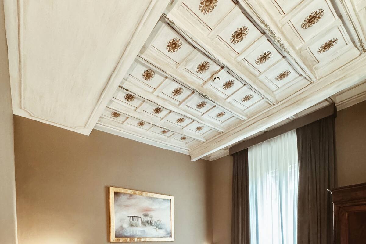 A hotel room with two beds, a painting on the wall, and a large window with curtains.