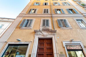 A building facade with a large central door, multiple windows with shutters, and a sign reading "FARMACIA DEL CORSO".