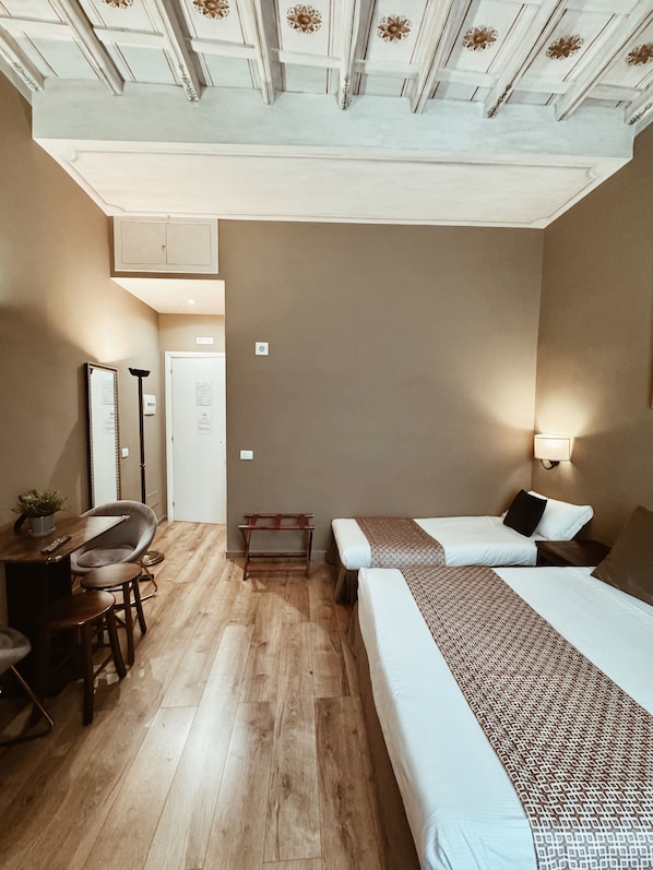 A hotel room with two beds, a desk, a chair, and a small table.