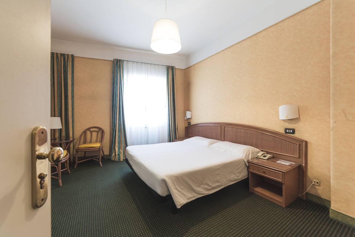 Ein Hotelzimmer mit einem großen Bett, einem Holznachttisch, einem Sessel und einem Schreibtisch.