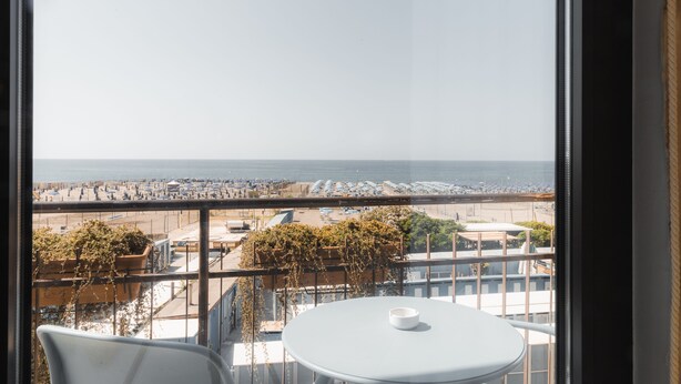 A balcony with a table and chairs, overlooking a beach with umbrellas and a parking lot. - Albergo Santa Maria (Chiavari)