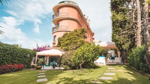 A building with a curved facade, a covered outdoor seating area, and a well-maintained garden with stepping stones. - Albergo Santa Maria (Chiavari)