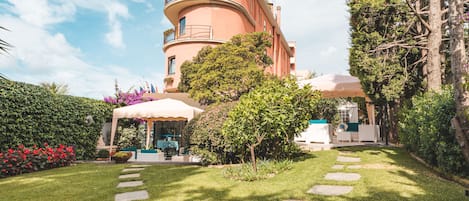 A building with a curved facade, a covered outdoor seating area, and a well-maintained garden with stepping stones.