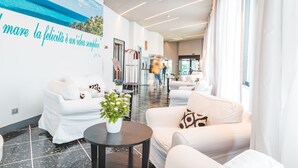 A modern hotel lobby with white sofas, a potted plant, and a mural of the sea. - Albergo Santa Maria (Chiavari)