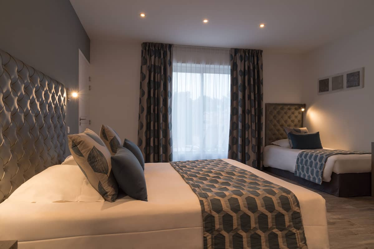 A hotel room with a large bed, a smaller bed, and a headboard with a textured design.