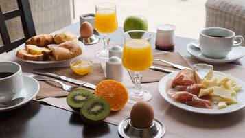 A breakfast table with croissants, orange juice, kiwi, cheese, and ham.